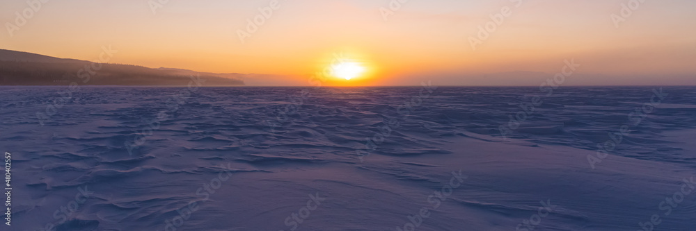 Winter frozen lake scene in northern Canada on a stunning clear morning sunrise in January with white snow on a frozen lake and iconic Canadian landscape in the north in panoramic photo. 
