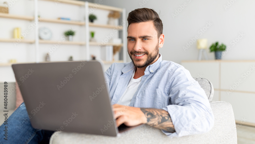 Positive guy reclining on sofa with laptop at home interior, urfing internet or scrolling social networks, panorama Positive guy reclining on sofa with laptop at home interior, urfing internet or scrolling social networks, panorama