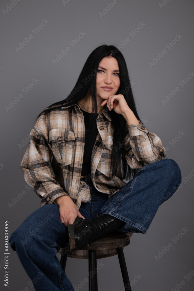 portrait of beautiful young woman in brown checkered shirt and jeans on gray background. pretty female portrait. portrait of beautiful young woman in brown checkered shirt and jeans on gray background. pretty female portrait.