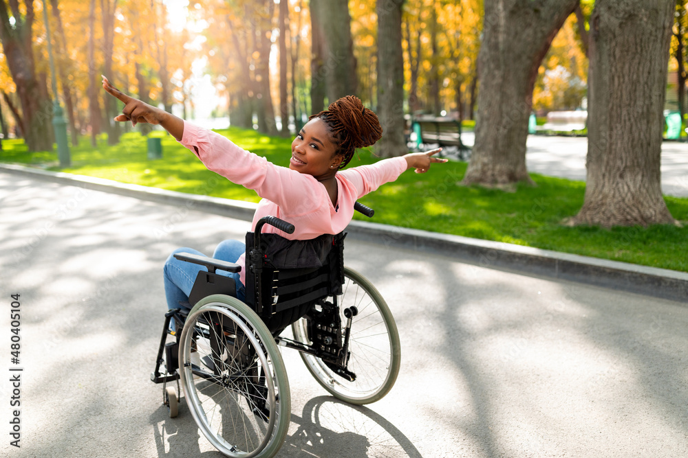 Young disabled black woman in wheelchair spreading arms, making victory gesture, feeling free at autumn park Young disabled black woman in wheelchair spreading arms, making victory gesture, feeling free at autumn park