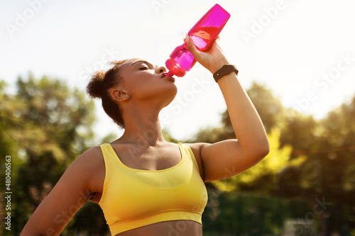 Fit black woman in yellow sportswear drinking water