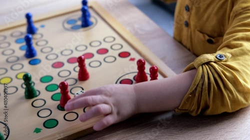 close-up of hands of small child manipulate with wooden figurines of family board game, smart kid, 2-year-old girl is learning to count, Cross and circle game Parcheesi, foreground focus