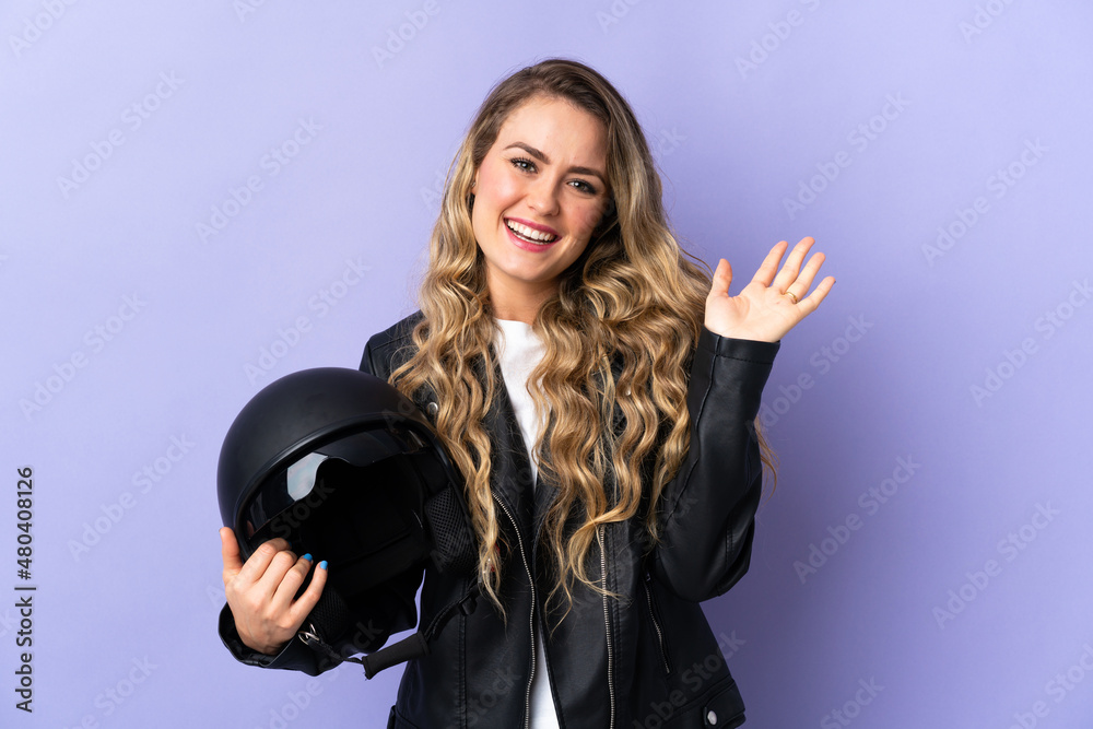 Young Brazilian woman holding a motorcycle helmet isolated on purple background saluting with hand with happy expression Young Brazilian woman holding a motorcycle helmet isolated on purple background saluting with hand with happy expression