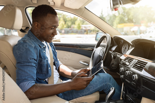 Positive black guy using digital tablet while driving car © Prostock-studio