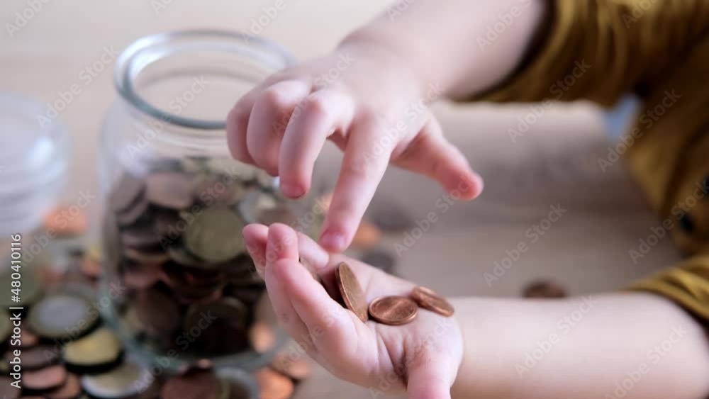 close-up of hands of small child manipulate with metal coins, kid counts, puts euro union money in piggy bank, glass jar, concept of pocket money, life insurance, save up for gift close-up of hands of small child manipulate with metal coins, kid counts, puts euro union money in piggy bank, glass jar, concept of pocket money, life insurance, save up for gift