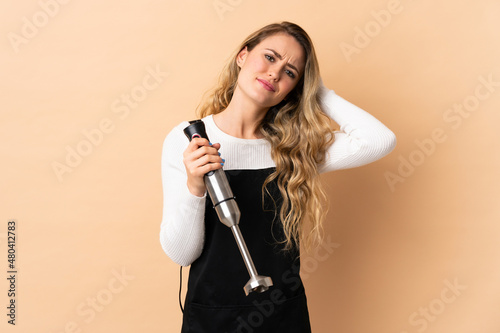 Young brazilian woman using hand blender isolated on beige background having doubts