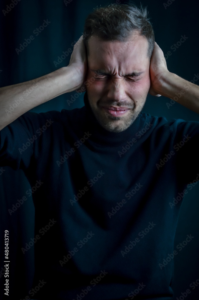portrait of a young man with his hands covering his ears not to hear and his eyes closed, disturbed by the noise
