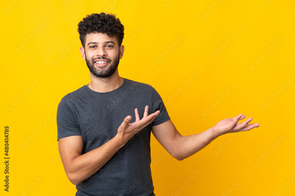 Young Moroccan man isolated on yellow background extending hands to the side for inviting to come Young Moroccan man isolated on yellow background extending hands to the side for inviting to come