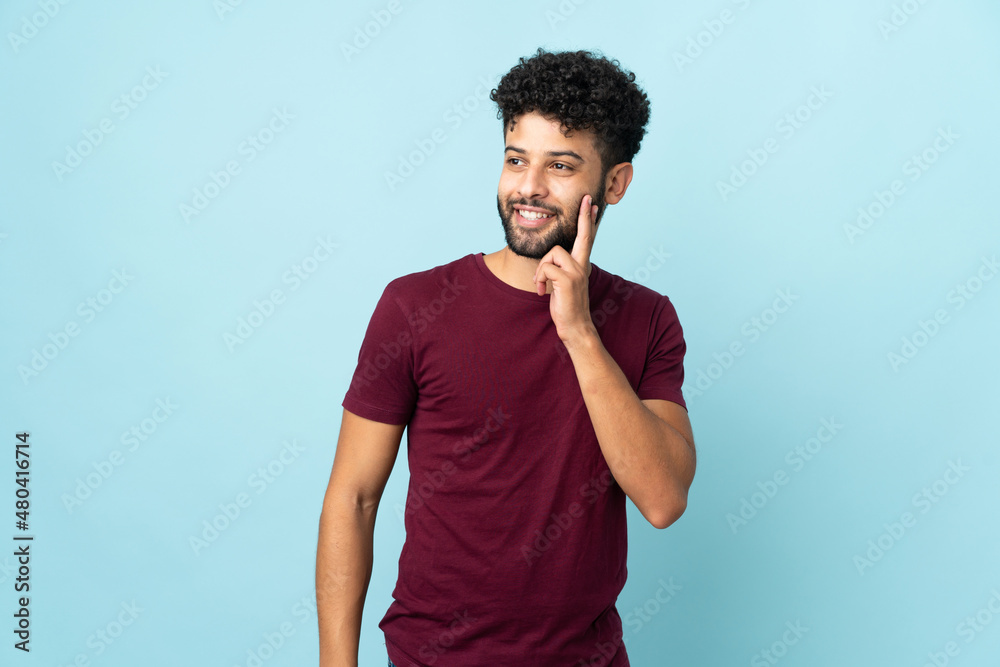 Young Moroccan man isolated on blue background thinking an idea while looking up