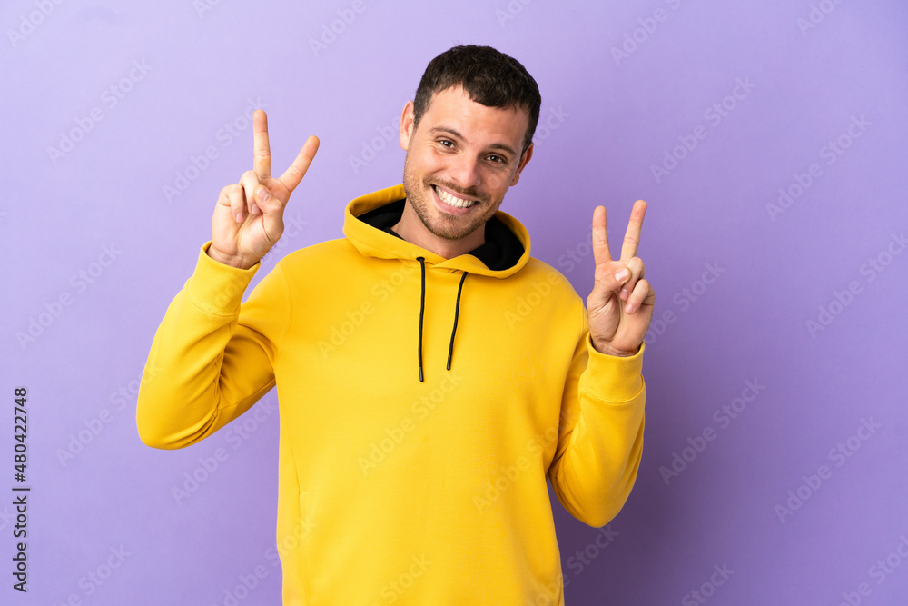 Brazilian man over isolated purple background showing victory sign with both hands Brazilian man over isolated purple background showing victory sign with both hands