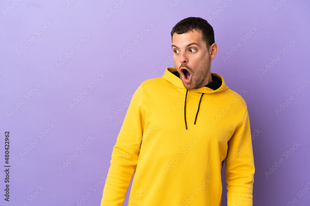 Brazilian man over isolated purple background doing surprise gesture while looking to the side Brazilian man over isolated purple background doing surprise gesture while looking to the side