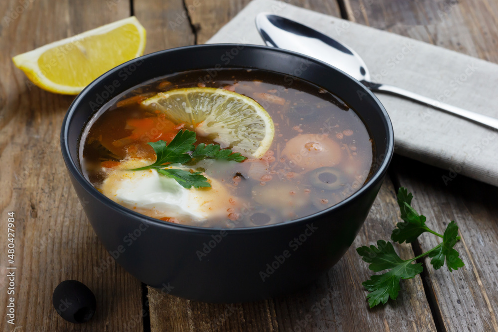 Traditional russian meat soup Solyanka in a black bowl