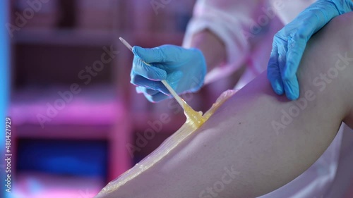 beautician is removing hair from leg of client using sugaring paste, sugar waxing
