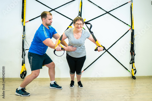 an elderly woman monitors her physical health. Granny goes in for sports under the guidance of a coach. A modern, advanced grandmother does trx exercises. fitness © Ольга Новицкая