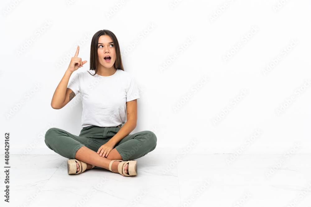 Teenager girl sitting on the floor intending to realizes the solution while lifting a finger up