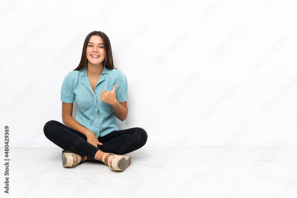 Teenager girl sitting on the floor pointing to the side to present a product Teenager girl sitting on the floor pointing to the side to present a product