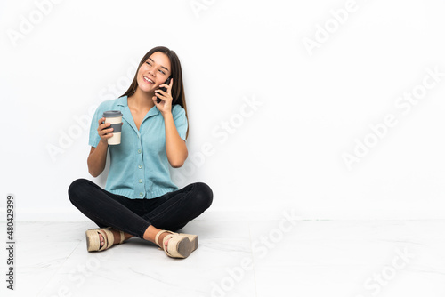 Teenager girl sitting on the floor holding coffee to take away and a mobile