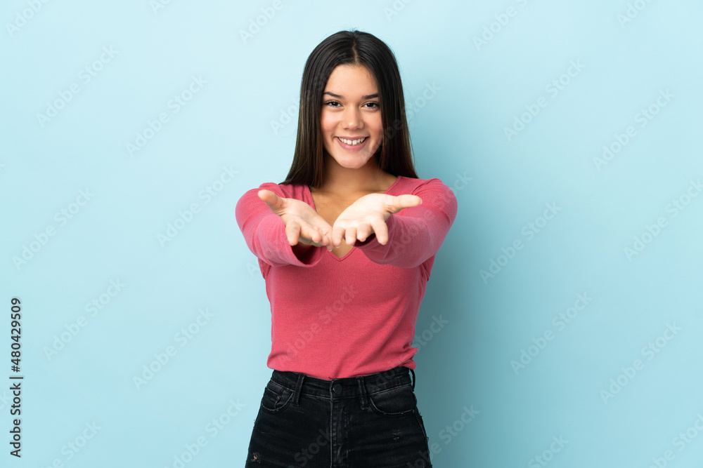 Teenager girl isolated on blue background holding copyspace imaginary on the palm to insert an ad Teenager girl isolated on blue background holding copyspace imaginary on the palm to insert an ad