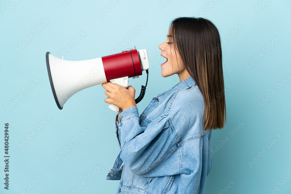 Teenager girl isolated on yellow background shouting through a megaphone to announce something in lateral position Teenager girl isolated on yellow background shouting through a megaphone to announce something in lateral position