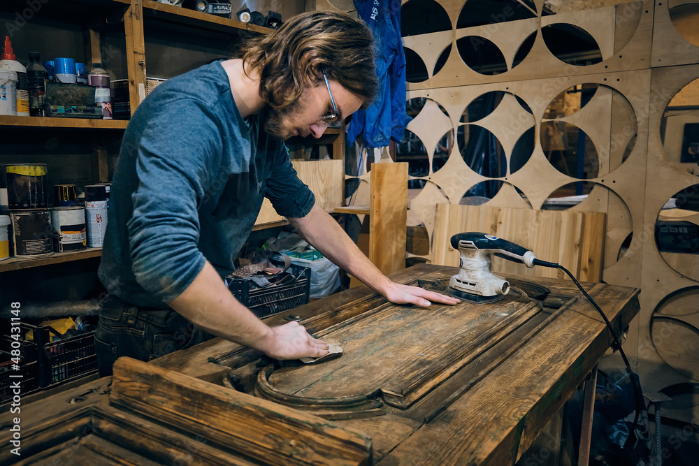 Carpenter sands wooden door with sandpaper and sanding machine