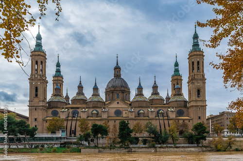 Cathedral-Basilica of Our Lady of the Pillar on the embankment of Ebro river with yellow water in Zaragoza on an autumn day  Spain. Panoramic view of the Spanish Roman Catholic Church