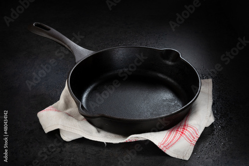 Empty cast iron pan on kitchen cloth and black background and between shadow photo