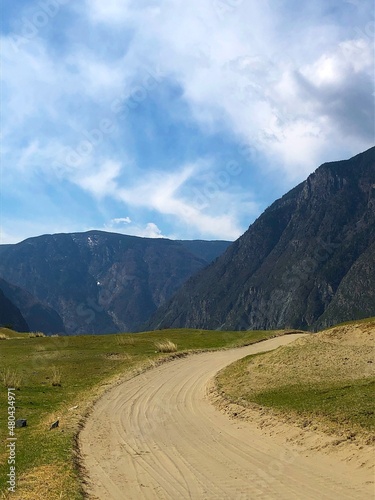 A road without asphalt, a primer among the mountains in spring and a blue sky with clouds