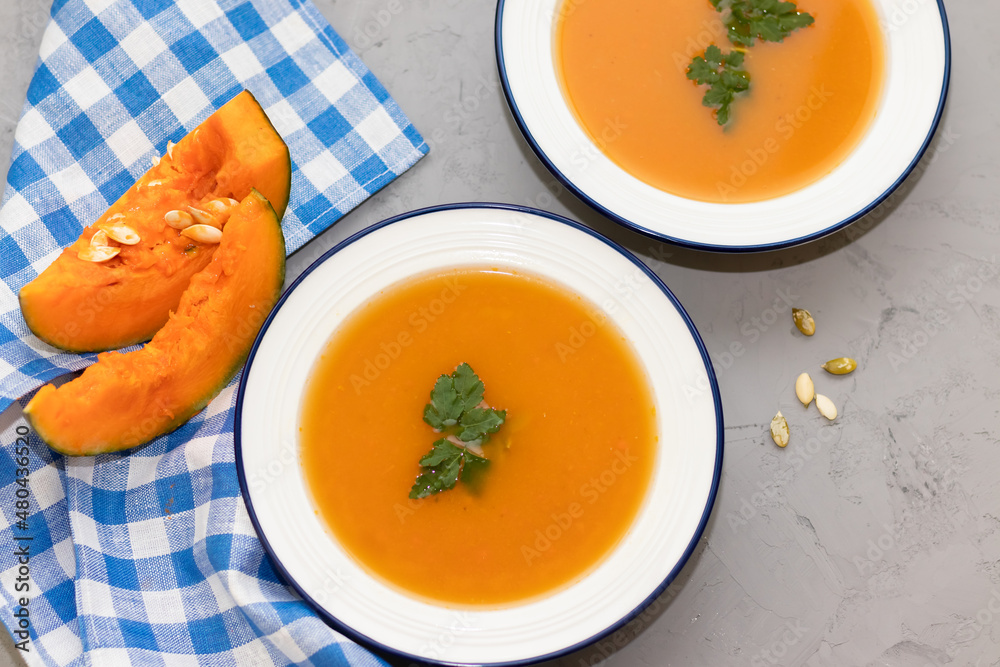 two plates of pumpkin soup on a concrete background and a napkin in a checkered blue two plates of pumpkin soup on a concrete background and a napkin in a checkered blue