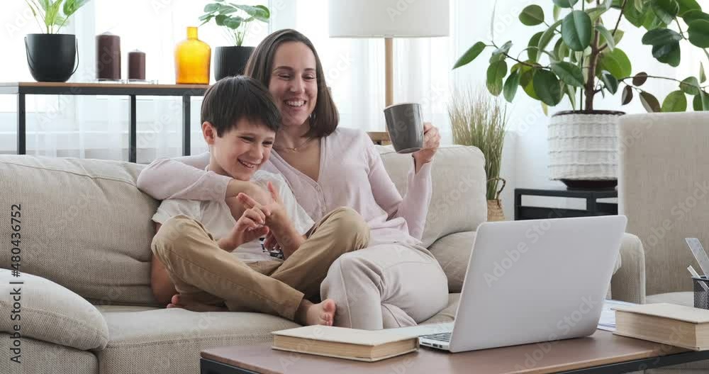 Woman drinking coffee while watching funny movie on laptop with her son at home Woman drinking coffee while watching funny movie on laptop with her son at home