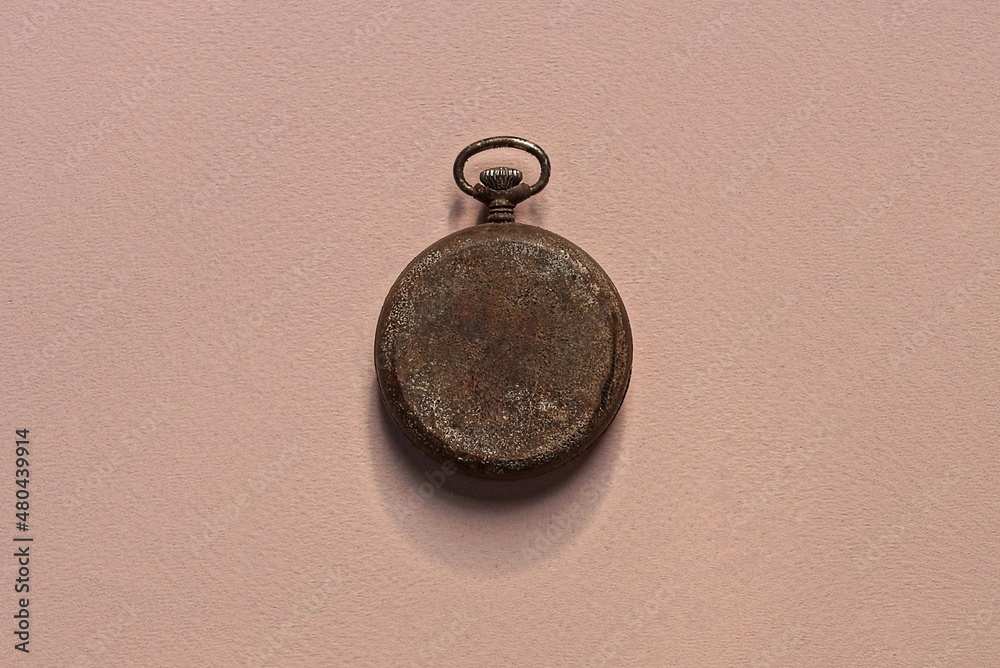 one old pocket watch with a gray metal cover lies on a brown table