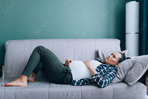 Sad depressed pregnant woman lying on couch in living room and looking at the ceiling. Loneliness, single mother, unwanted baby © Olga