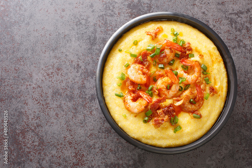 Homemade shrimp and grits with smoked bacon, onions and cheese in a black bowl on a dark concrete background. American cuisine. Horizontal top view from above