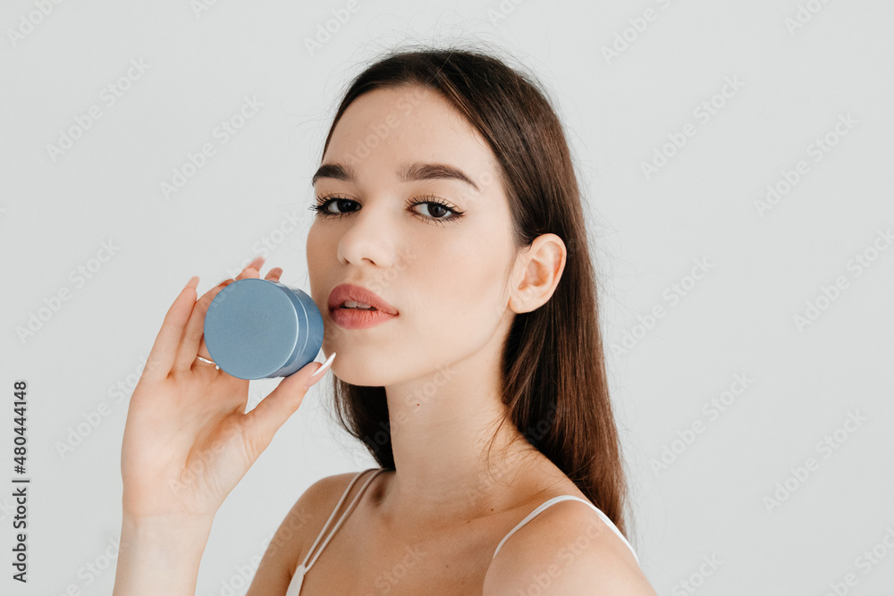 Pretty young woman with clean perfect skin holding blue jar with cosmetic cream on white background Pretty young woman with clean perfect skin holding blue jar with cosmetic cream on white background