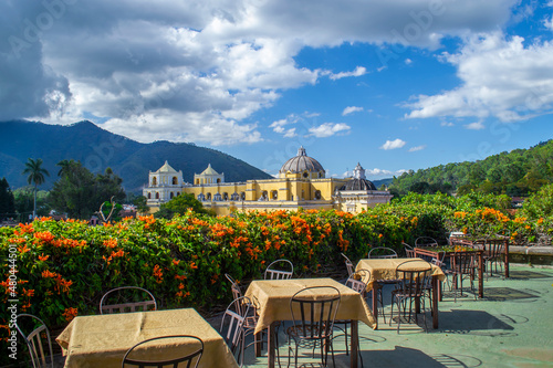 Restaurant tables on an outdoor terrace overlooking the mountainous natural landscape, volcano and an old church as architectural work. 
