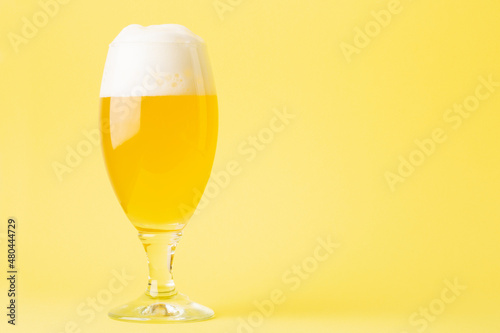 A glass of wheat beer on a yellow background with copy space