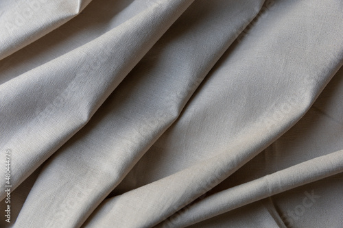 Textured folds of linen fabric in beige color. Textile background, top view. Organic cloth