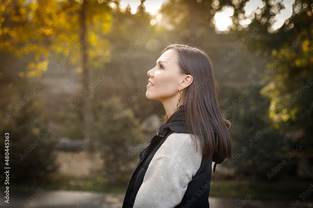 Profile of a young smiling woman with autumn in a park outdoors in a warm beige jacket and a black sleeveless jacket. Profile of a young smiling woman with autumn in a park outdoors in a warm beige jacket and a black sleeveless jacket.