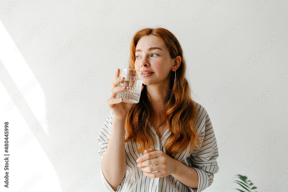 Lovely cheerful woman maintaining her water balance, holding a glass of pure water, looking Lovely cheerful woman maintaining her water balance, holding a glass of pure water, looking
