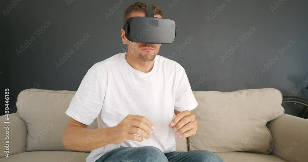 Man sitting on couch, using Virtual Reality headset, gesturing with fingers. Man sitting on couch, using Virtual Reality headset, gesturing with fingers.