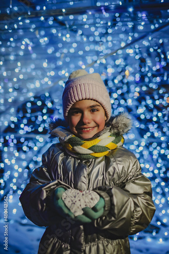 Happy girl holding a crafted heart to present at Valentine Day or Christmas over blue blurred lights, authentic lifestyle in winter city