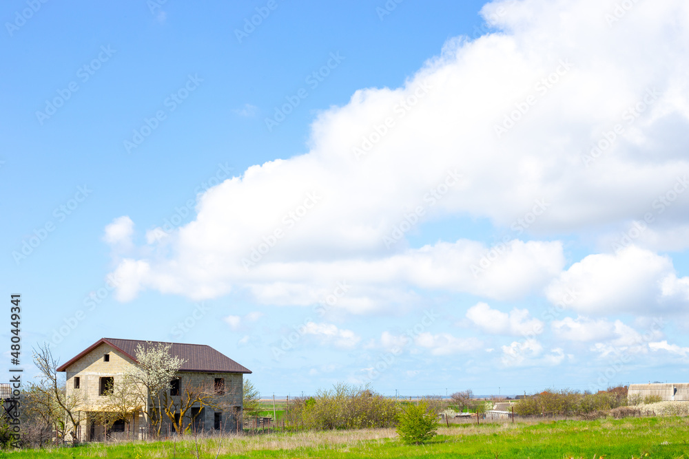 Rural landscape. House under construction in the village and blue sky with clouds on a sunny spring day