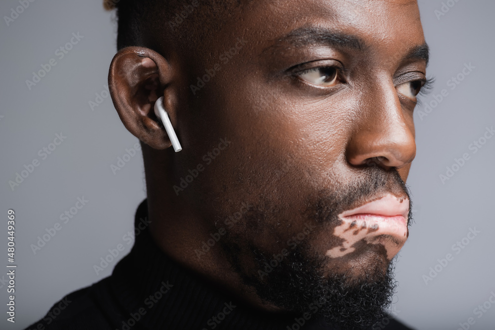 Obraz premium close up portrait of african american man with vitiligo listening music in earphone isolated on grey.