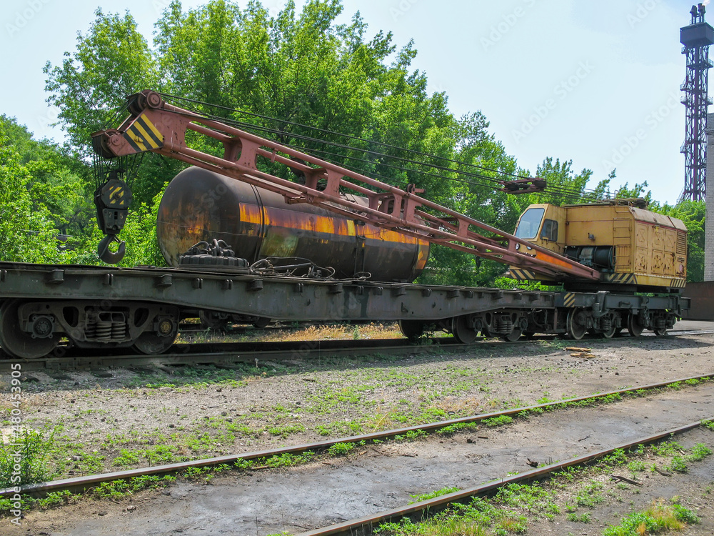 Naklejka premium railway crane with a platform under the boom stands on the railway tracks near the locomotive depot 