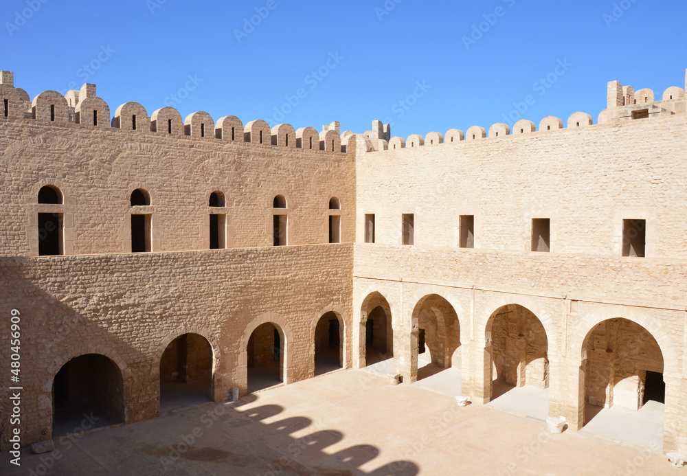 The inner yard of VIII century arabic fortress (ribat) in Sousse, Tunisia, Africa. Blue sky, old arches, shadows and sunlight on the ancient stone walls