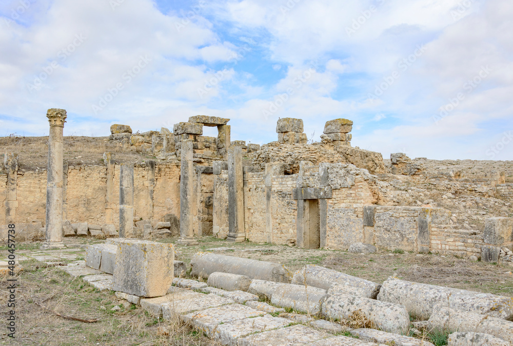 Ruins of the antique Roman city of Thugga in Tunisia, Africa. Yellow and grey stone standing and lying ruined columns, blue sky with clouds