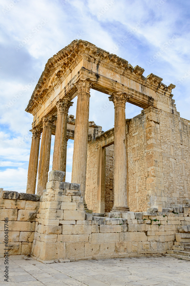 Obraz premium Temple of Jupiter, forum and ancient roman ruins of Dougga in Tunisia, Africa in the sunny afternoon. Blue sky with clouds, old yellow, grey and brown stone walls and columns 
