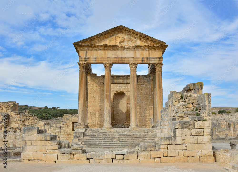 Temple of Jupiter, forum  and ancient roman ruins of Dougga in Tunisia, Africa in the sunny afternoon. Blue sky with clouds, old yellow, grey and brown stone walls and columns 