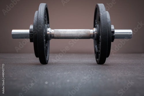 A dumbbell bar loaded with weight plates on the floor at the gym. Bodybuilding equipment on a clean background with empty space for text. Fitness, weight training or healthy lifestyle concept