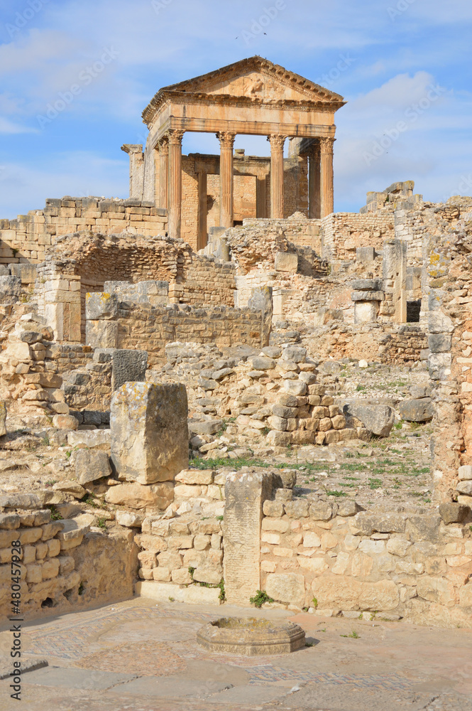 Fototapeta premium Temple of Jupiter and ancient roman ruins of Dougga in Tunisia, Africa in the sunny afternoon. Blue sky with clouds, old yellow, grey and brown stone walls and columns 