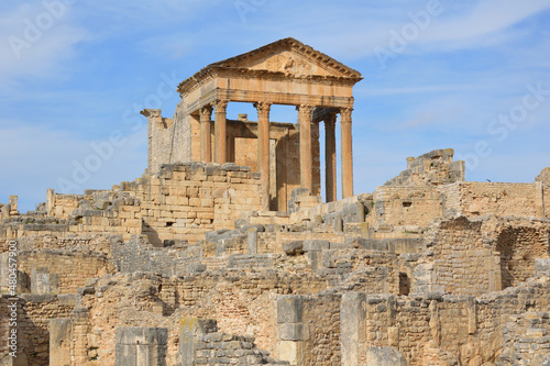 Temple of Jupiter and ancient roman ruins of Dougga in Tunisia, Africa in the sunny afternoon. Blue sky with clouds, old yellow, grey and brown stone walls and columns 